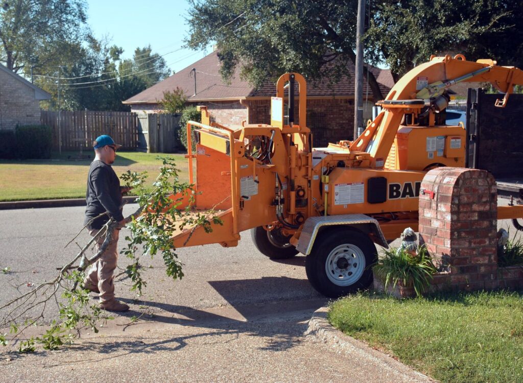 Worker feeding brush into a wood chipper in a residential driveway